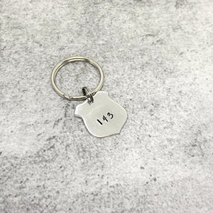 May include: Silver keychain with a shield-shaped charm engraved with the number "143".