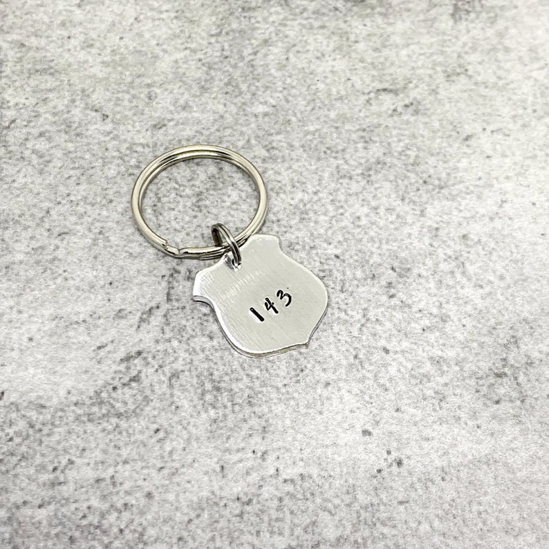 May include: Silver keychain with a shield-shaped charm engraved with the number "143".