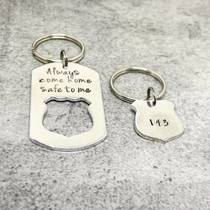 May include: A silver keychain with a badge-shaped charm that says "Always come home safe to me". A second silver keychain with a smaller badge-shaped charm that says "143".