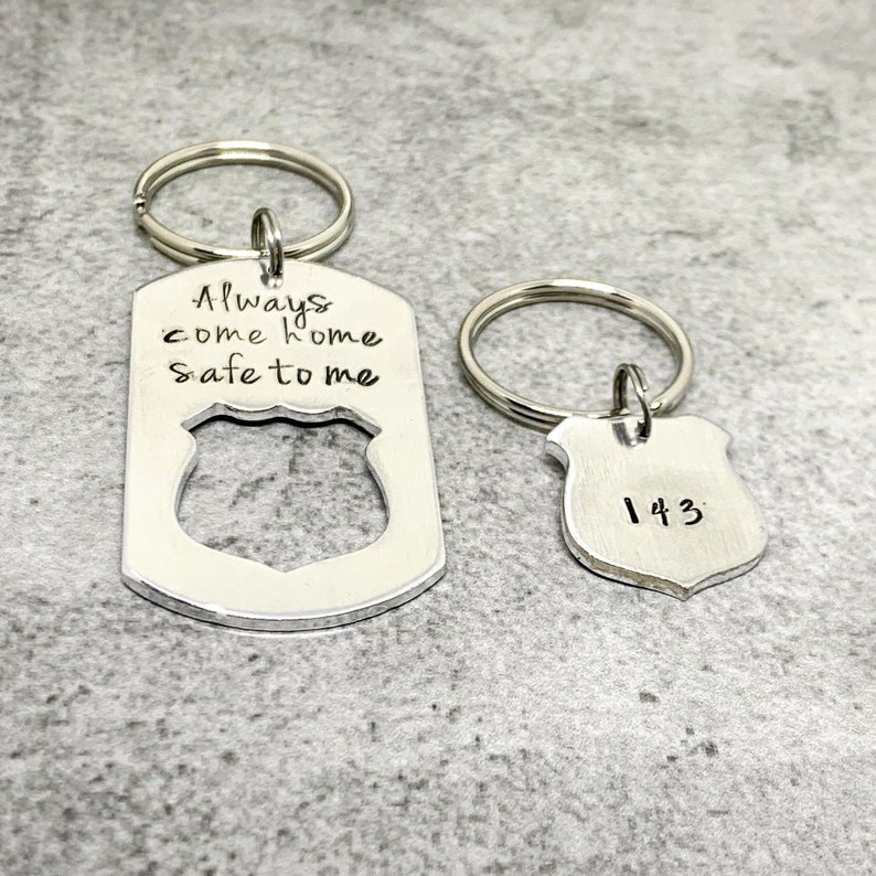 May include: A silver keychain with a badge-shaped charm that says "Always come home safe to me". A second silver keychain with a smaller badge-shaped charm that says "143".