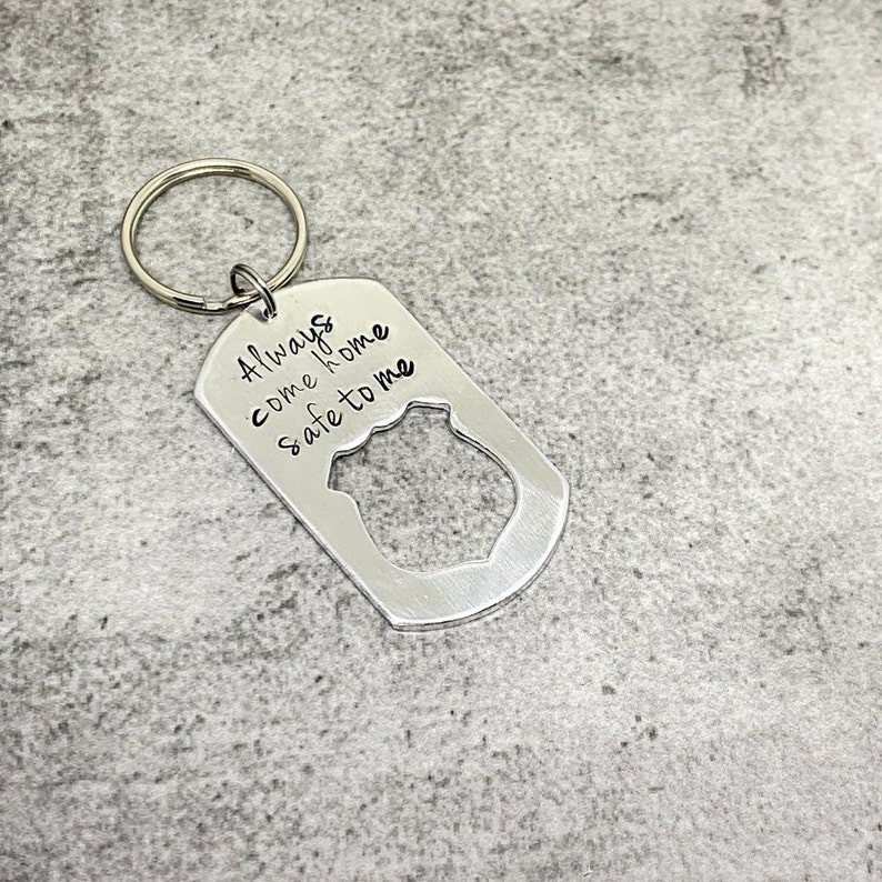 May include: Silver keychain with a police badge cutout and the inscription "Always come home safe to me".