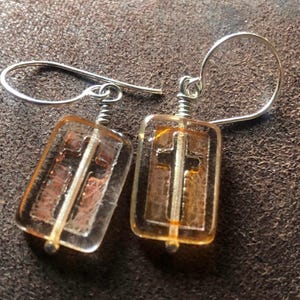 May include: A pair of silver earrings with amber glass cross charms. The cross is outlined in silver and the glass has a textured surface.