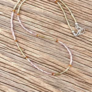 May include: A delicate necklace with alternating pink and gold beads. The necklace has a silver clasp.
