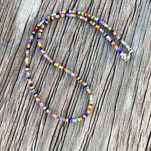 May include: A colorful beaded necklace with a silver clasp. The beads are small and round, and they are arranged in a random pattern. The necklace is on a wooden background.