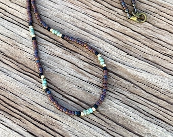 May include: A brown beaded necklace with turquoise, black, and gold accents. The necklace has a lobster clasp closure.