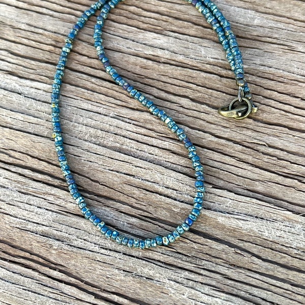 Op de afbeelding: Een tealblauwe ketting gemaakt van kleine vierkante kralen met een zilveren sluiting.