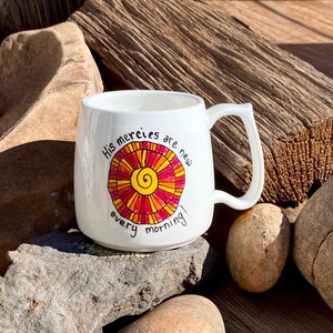 May include: White ceramic mug with a colourful sun design and the text "His mercies are new every morning!"
