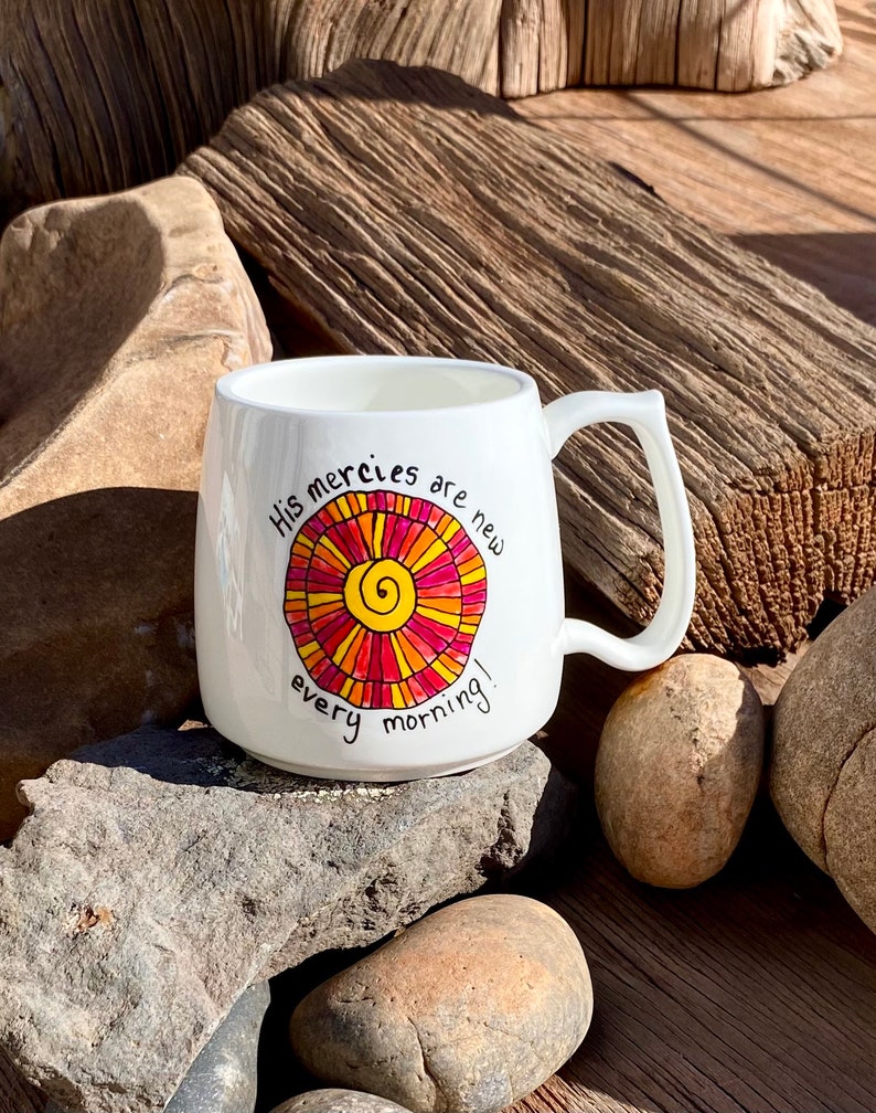 May include: White ceramic mug with a colourful sun design and the text "His mercies are new every morning!"