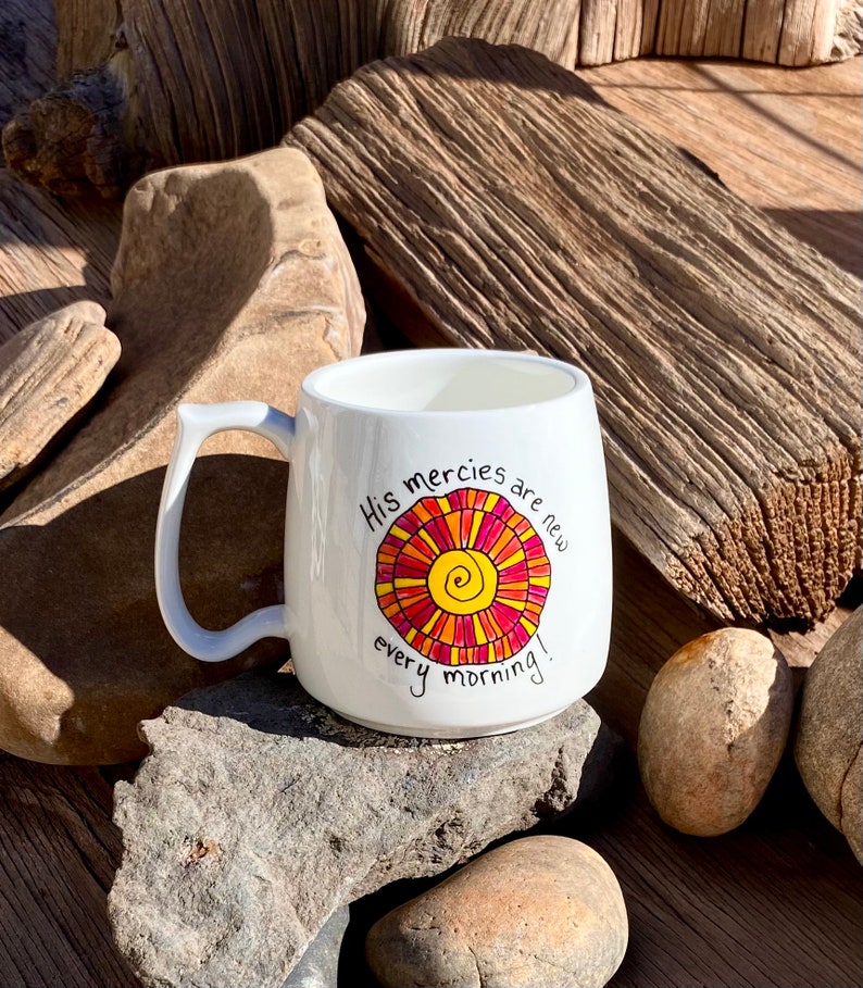 May include: White ceramic mug with a colourful sun design and the text "His mercies are new every morning!"