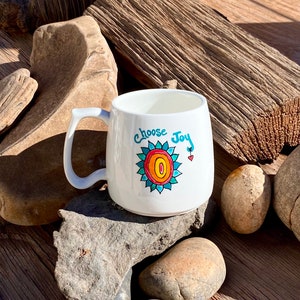 May include: White ceramic mug with a blue, orange and red sunflower design and the text "Choose Joy".