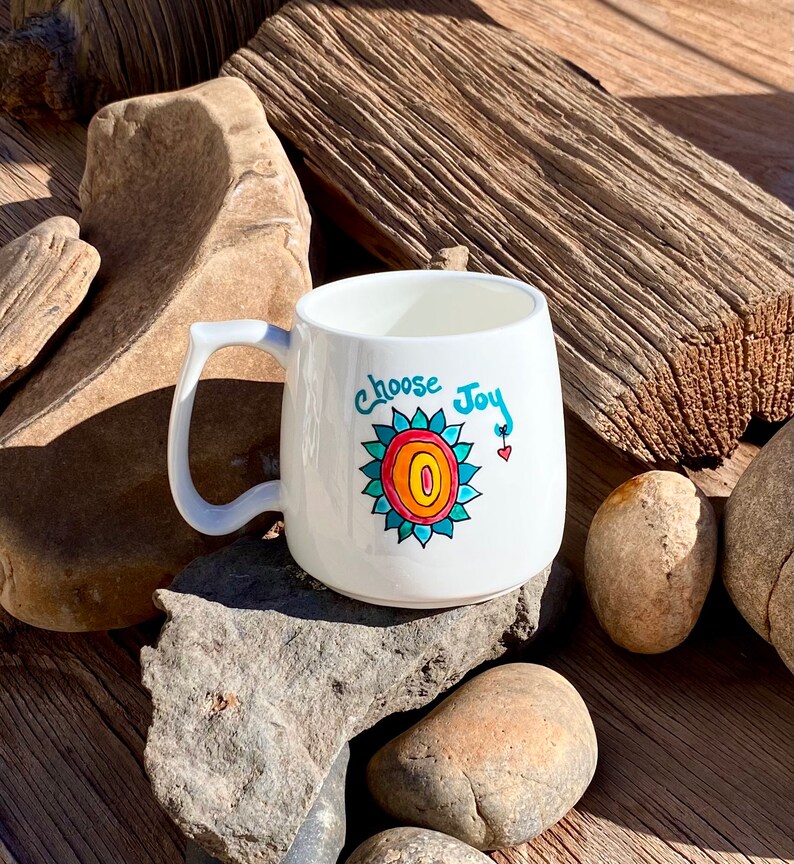May include: White ceramic mug with a blue, orange and red sunflower design and the text "Choose Joy".