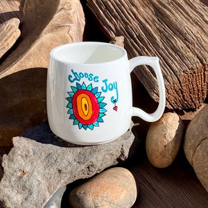 May include: White ceramic mug with a colourful hand-painted design of a flower and the words "choose joy".