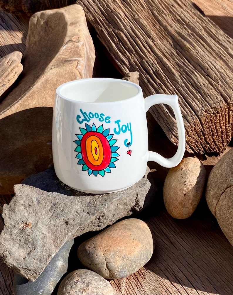 May include: White ceramic mug with a colourful hand-painted design of a flower and the words "choose joy".