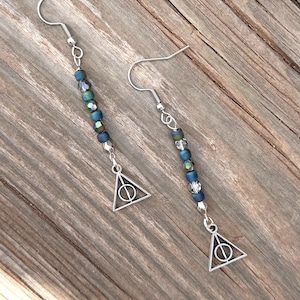 May include: A pair of dangle earrings featuring silver-toned fishhook wires, a vertical strand of iridescent blue and clear faceted beads, and a silver-toned metal charm shaped like a triangle with an inscribed circle and vertical line.