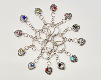 May include: A set of 10 silver keychains with heart-shaped charms. Each charm features a different colored rhinestone in the center. The keychains are connected by a series of interlocking rings.
