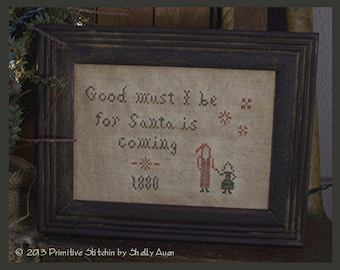 May include: A framed cross-stitch sampler with the text "Good must be for Santa is coming 1880". The sampler features a red and white Santa Claus figure and a child holding a small gift.