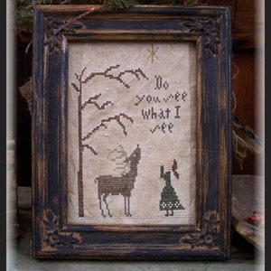 May include: A framed cross-stitch design featuring a girl and a deer in a snowy forest. The text reads "Do you see what I see".