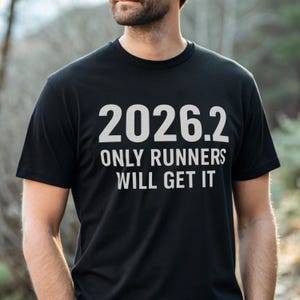 以下が含まれることがあります： 白文字で「2026.2 ONLY RUNNERS WILL GET IT」と書かれた黒いTシャツ。クルーネックのTシャツは柔らかい素材でできています。テキストは前面の中央に配置されています。テキストはマラソンの距離を指します。