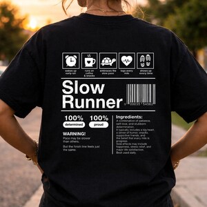 May include: Black t-shirt with white text and graphics. The shirt says "Slow Runner" with a list of "ingredients" and icons. The icons include a clock, coffee cup, turtle, heartbeat, and footprints.
