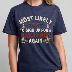 Könnte beinhalten: Marineblaues T-Shirt mit dem Text "MOST LIKELY TO SIGN UP FOR A MARATHON AGAIN" in Weiß und Rot. Das Design umfasst Weihnachtsmannfiguren und festliche Elemente.