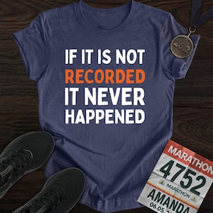 May include: Navy blue t-shirt with the text "IF IT IS NOT RECORDED IT NEVER HAPPENED" in white and orange. Includes a marathon medal, running shoes, and a marathon bib.