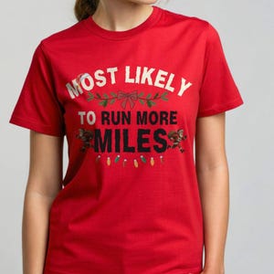 May include: Red t-shirt with the text "MOST LIKELY TO RUN MORE MILES" in white. The design includes festive elements like a Santa hat, a bow, and running Santas. A string of colorful lights is at the bottom.