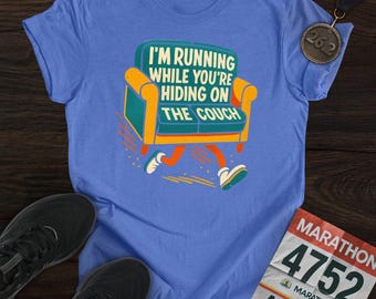 May include: A light blue t-shirt featuring the text "I'M RUNNING WHILE YOU'RE HIDING ON THE COUCH" and a cartoon couch design. The image includes black running shoes, a marathon medal, and a race bib.