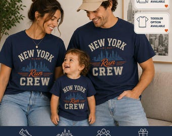 May include: A navy blue short-sleeve t-shirt featuring a graphic print that reads NEW YORK 26.2 MILES RUN CREW with a skyline silhouette. The design includes orange horizontal lines and beige lettering. A beige baseball cap is also visible.