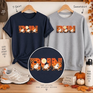 May include: A navy blue t-shirt and a gray sweatshirt, both featuring a graphic print of the word RUN with ghosts running through a forest scene. The design includes autumn leaves, bats, and a full moon. A matching water bottle and sneakers are present.