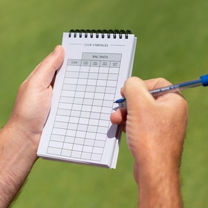 May include: A white spiral bound notebook with the title "Club Yardages" and a table labelled "Bag Data" with columns for "Club", "Stock Carry", "Max Carry", "Shot Shape", and "Usual Yardage".