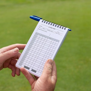 May include: A white golf scorecard with a blue pen on top. The scorecard has columns for each hole, with spaces for the player's score, putts, and other information.