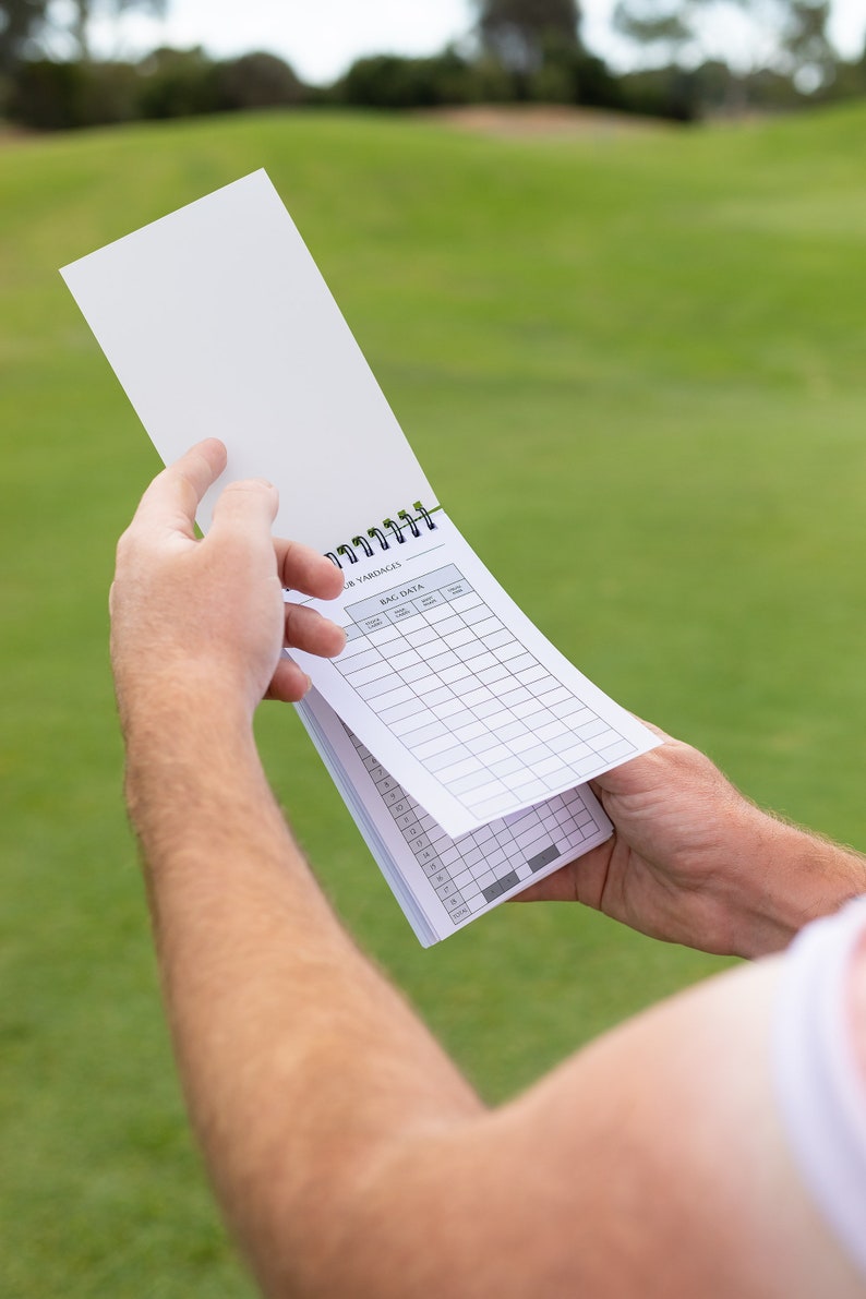 May include: A white golf scorecard with a black spiral binding. The scorecard has columns for each hole, with headings for "Yardages", "Par", "Score", "Putts", "Penalties", and "Total".