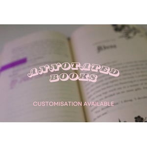 Könnte beinhalten: Nahaufnahme eines geöffneten Buches mit dem Text "ANNOTATED BOOKS" in rosa Buchstaben auf dem Buch. Der Text "CUSTOMISATION AVAILABLE" befindet sich unter dem Buch.
