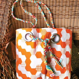 May include: A white and orange tote bag with a geometric pattern. The bag has two grommets with a braided fabric strap going through them. The strap is made of different colored fabrics, including red, yellow, blue, and green.