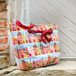 May include: A red and white quilted tote bag with a city skyline pattern. The bag has a red fabric handle with silver grommets.