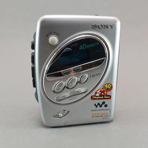 May include: Silver Sony Walkman with "MEGA BASS" and "40 PRESETS" text. Features buttons for FM/AM, preset, and hold. Includes a small display screen and a sticker indicating up to 25 hours of playback time.