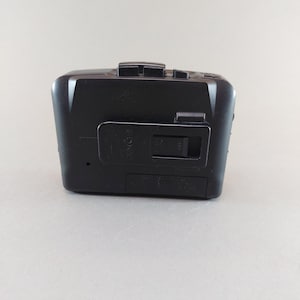 May include: A black Sony cassette player with a rectangular design. The player has several buttons on the top and a battery compartment on the bottom. The Sony logo is visible on the front.