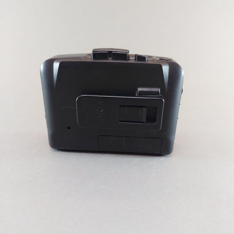 May include: A black Sony cassette player with a rectangular design. The player has several buttons on the top and a battery compartment on the bottom. The Sony logo is visible on the front.