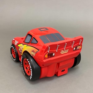 May include: Red toy car with black wheels and a spoiler. The car has the number 95 on the side and the word "Rust-eze" on the back.