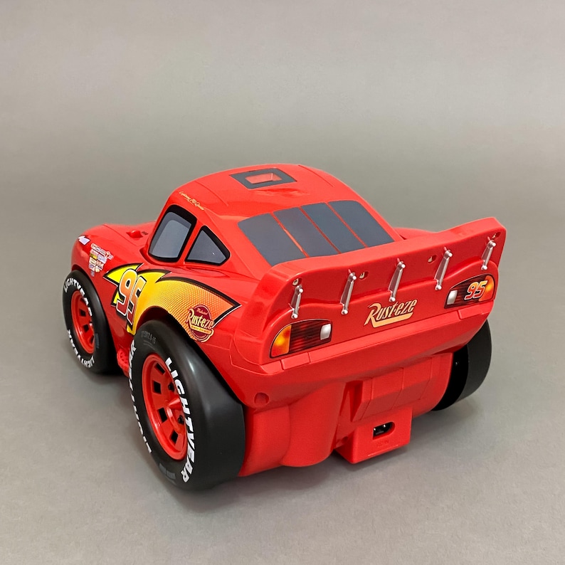 May include: Red toy car with black wheels and a spoiler. The car has the number 95 on the side and the word "Rust-eze" on the back.