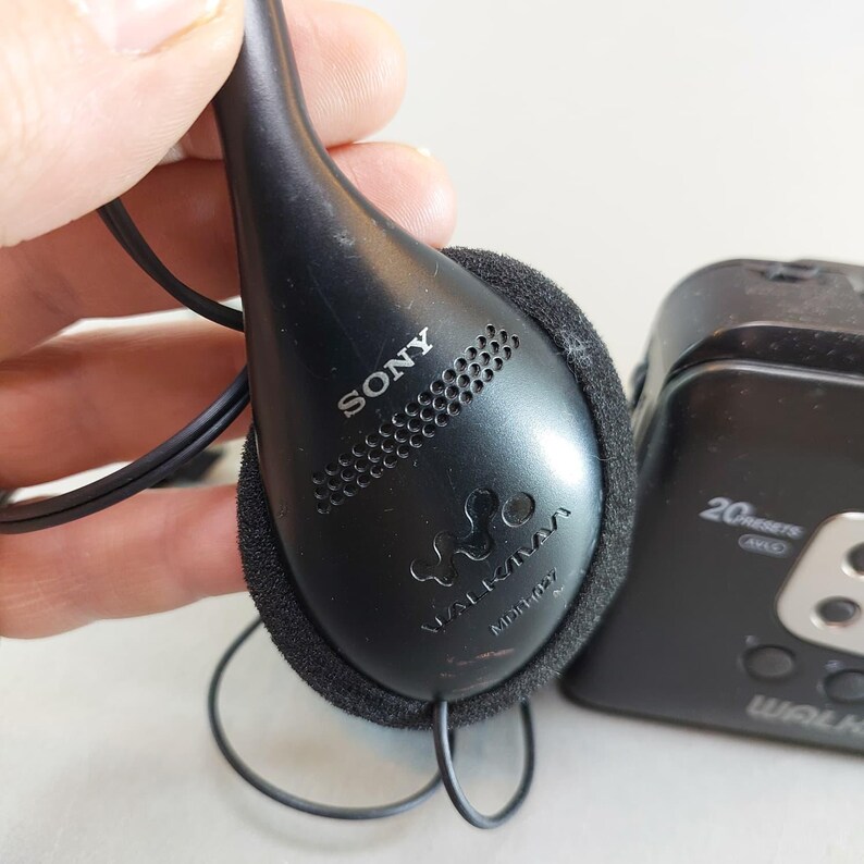 May include: Black Sony Walkman headphones with a foam ear cushion. The headphones are connected to a black Walkman player. The Sony logo and Walkman model number are visible on the headphones.
