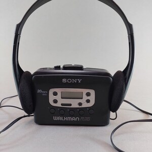 May include: Black Sony Walkman WM-FX221 with attached black headphones. The portable cassette player has a digital display and control buttons. The headphones have black ear pads. The Walkman is labeled with the Sony and Walkman logos.