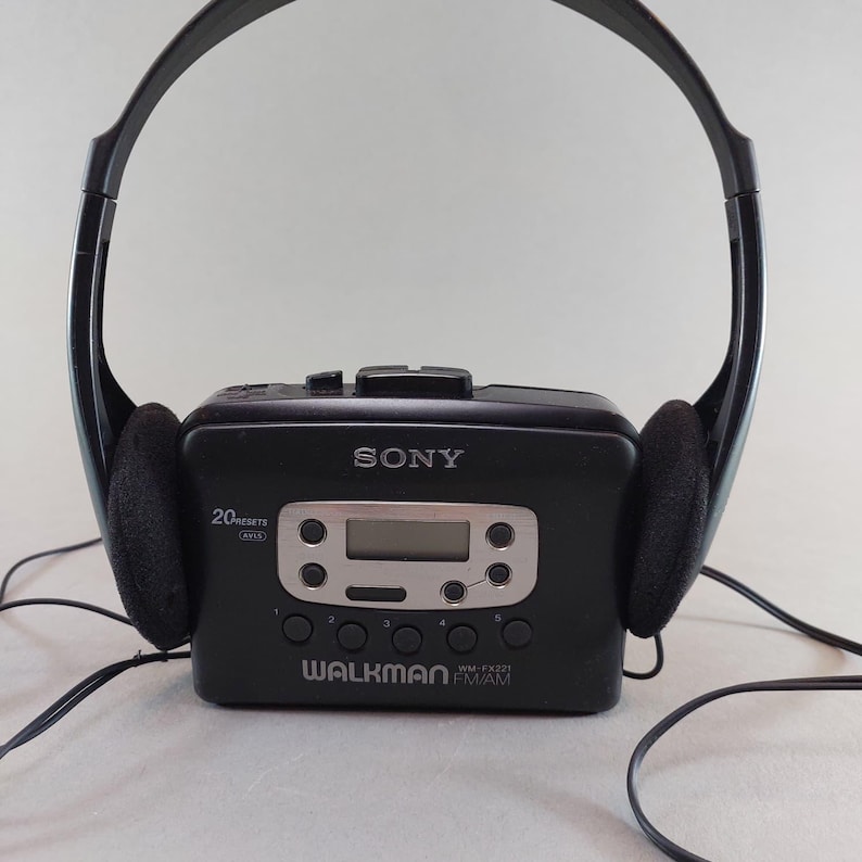 May include: Black Sony Walkman WM-FX221 with attached black headphones. The portable cassette player has a digital display and control buttons. The headphones have black ear pads. The Walkman is labeled with the Sony and Walkman logos.