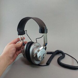 K&ouml;nnte beinhalten: Dynamischer Stereo-Kopfh&ouml;rer Sony DR-37 mit silbernen Ohrmuscheln, schwarzen gepolsterten Ohrpolstern und einem verstellbaren schwarzen Kopfb&uuml;gel. Das Ger&auml;t verf&uuml;gt &uuml;ber ein schwarzes Spiralkabel und silberne Metallb&uuml;gel mit sichtbaren Markierungen.