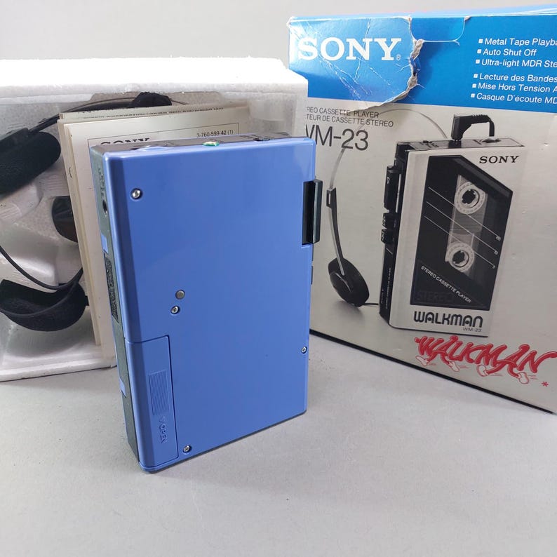 May include: A blue Sony Walkman WM-23 stereo cassette player with its original packaging box, white styrofoam insert, and black headphones. The box features the Sony logo, the model name, and illustrations of the device and headphones.