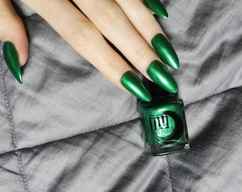 Może przedstawiać: Butelka zielonego lakieru do paznokci z czarną zakrętką i napisem "NU Nail Polish" na etykiecie. Butelka stoi na szarej powierzchni z tkaniny. W tle widać dłoń z długimi, zielonymi paznokciami.