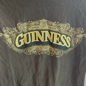 May include: A brown t-shirt with a gold Guinness logo. The logo features the words "Guinness", "Dublin", "Ireland", and "1759" in a decorative font.