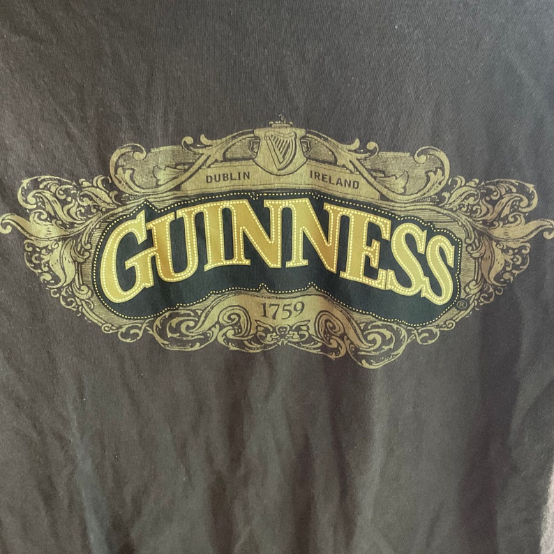 May include: A brown t-shirt with a gold Guinness logo. The logo features the words "Guinness", "Dublin", "Ireland", and "1759" in a decorative font.