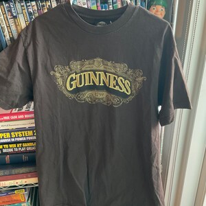 May include: A dark brown t-shirt with a gold and black Guinness logo. The logo features the words "Dublin" and "Ireland" and the year "1759".