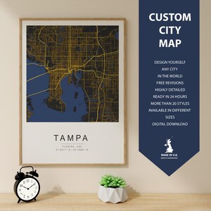 May include: A framed city map of Tampa, Florida, USA, with a gold grid over a blue background. The city name and coordinates are printed below. A navy blue banner on the right side reads "CUSTOM CITY MAP".